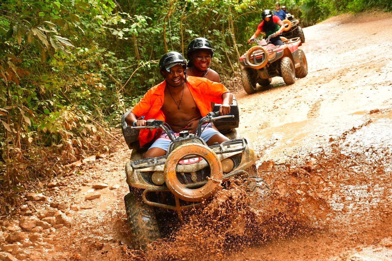 Paschal and Maryanne riding an ATV together on a muddy forest trail